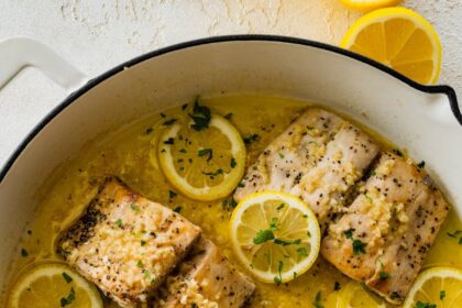 4 Mahi mahi fillets in a skillet with a lemon butter garlic sauce. There are lemon slices in the skillet and everything is topped with fresh parsley.