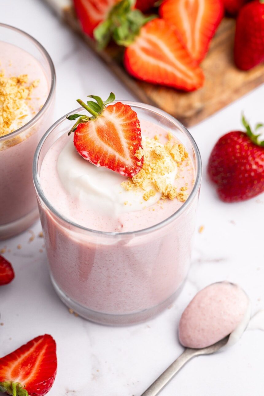 One glass filled with high-protein strawberry mousse topped with a dollop of cocowhip, one halved fresh strawberry and crushed graham crackers.