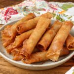 pottery plate stacked with lumpia next to napkin on table