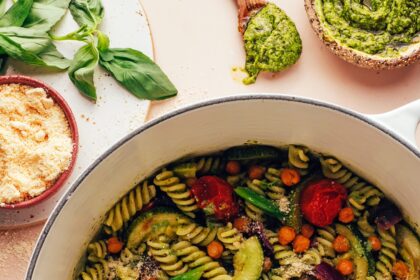 Bowl of vegan parmesan next to a Dutch oven filled with Zucchini Pesto Pasta with Roasted Tomatoes & Chickpeas