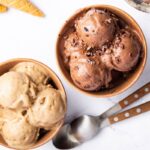 Two bowls of protein ice cream-one is chocolate and one is vanilla. There are two spoons next to the bowls.