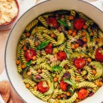 Bowl of vegan parmesan next to a Dutch oven filled with Zucchini Pesto Pasta with Roasted Tomatoes & Chickpeas