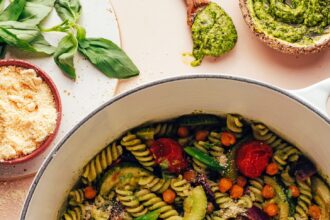 Bowl of vegan parmesan next to a Dutch oven filled with Zucchini Pesto Pasta with Roasted Tomatoes & Chickpeas