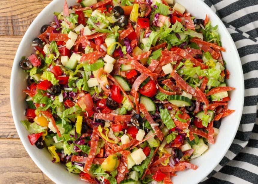 horizontal overhead photo of a loaded salad with salami and cheese