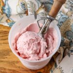 horizontal photo of ice cream in container with scoop on wooden table