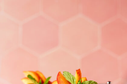 Two glasses of our frozen peach daiquiri on a plate with peach slices