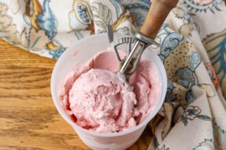 horizontal photo of ice cream in container with scoop on wooden table