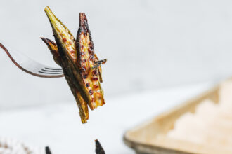 Fork holding up a few slices of crispy oven roasted okra over a plate of more baked okra