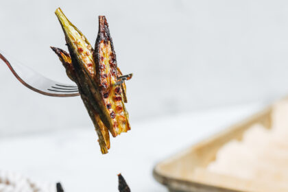 Fork holding up a few slices of crispy oven roasted okra over a plate of more baked okra