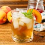 glass of tea on table with a sprig of mint and peach wedge