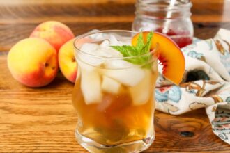 glass of tea on table with a sprig of mint and peach wedge