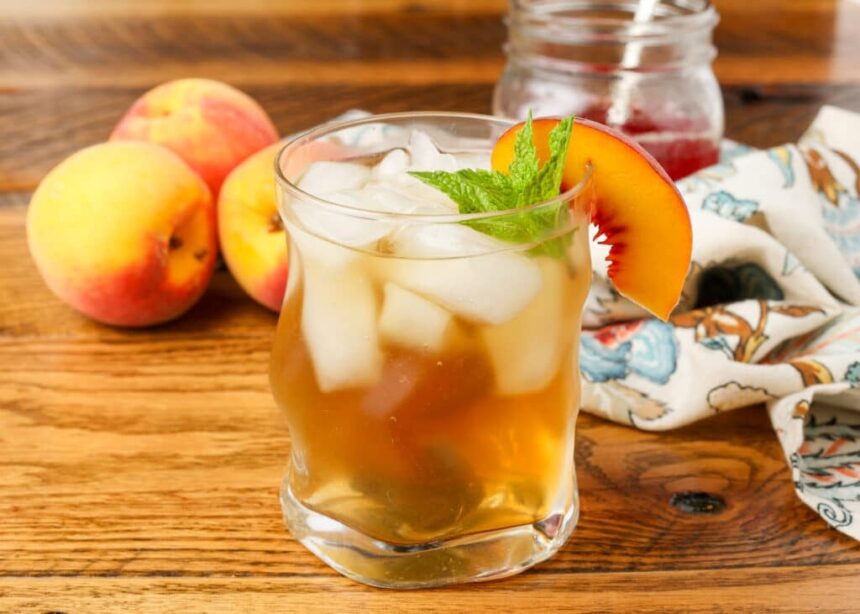 glass of tea on table with a sprig of mint and peach wedge
