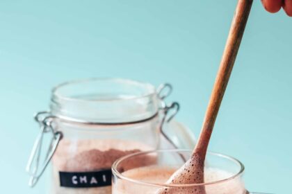 Using a small wooden spoon to make a mug of chai next to a small bowl and jar of Instant Chai Latte Mix