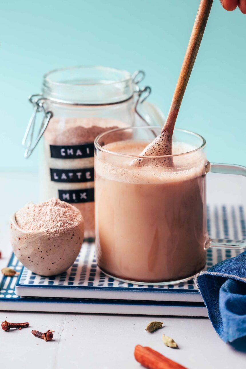 Using a small wooden spoon to make a mug of chai next to a small bowl and jar of Instant Chai Latte Mix
