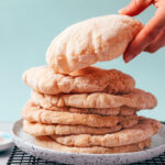 Hand reaching in to pick up a piece of gluten-free pita from a stacked plate of pita