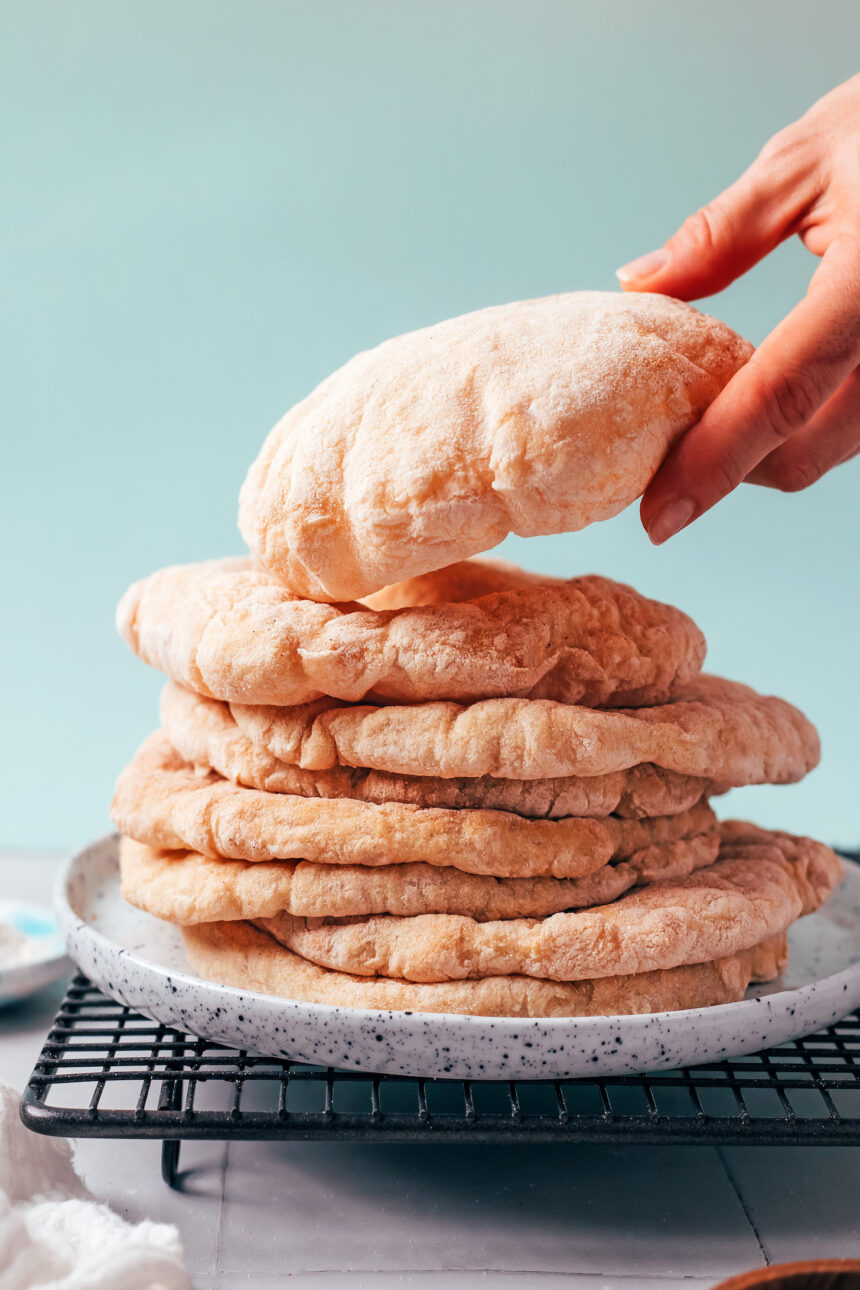 Hand reaching in to pick up a piece of gluten-free pita from a stacked plate of pita
