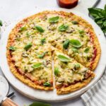 Whole chicken crust pizza topped with fresh basil. One slice has been cut from the crust.