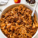 Bowl of shredded apple BBQ chicken with a serving spoon.