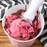 Cranberry Ice Cream being scooped out of a freezer safe container.