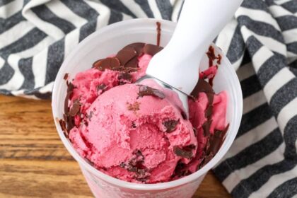 Cranberry Ice Cream being scooped out of a freezer safe container.