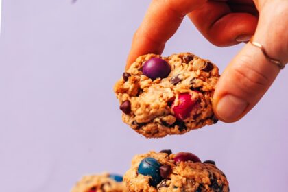 Picking up a vegan gluten-free oatmeal monster cookie from a stack of more cookies