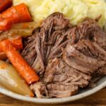 A horizontally aligned image of a ceramic plate piled high with tender roast beef, soft carrots, and a mountain of mashed potatoes.