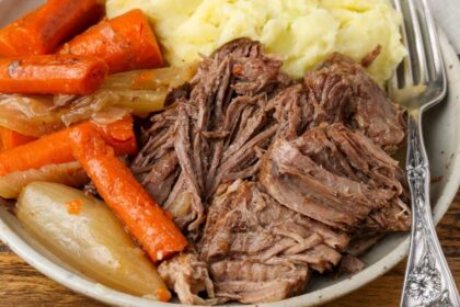 A horizontally aligned image of a ceramic plate piled high with tender roast beef, soft carrots, and a mountain of mashed potatoes.