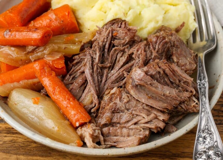 A horizontally aligned image of a ceramic plate piled high with tender roast beef, soft carrots, and a mountain of mashed potatoes.