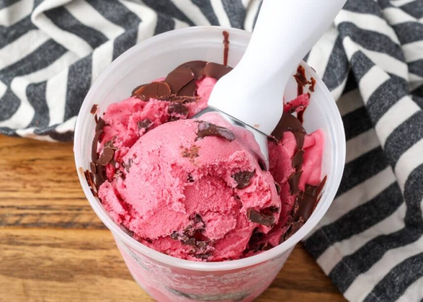 Cranberry Ice Cream being scooped out of a freezer safe container.