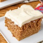 A slice of Crazy Spice Cake sits on a square white plate over a wooden tabletop.