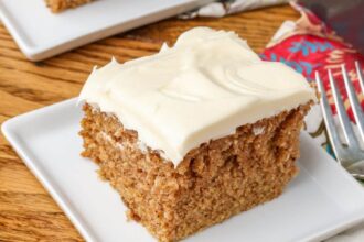 A slice of Crazy Spice Cake sits on a square white plate over a wooden tabletop.