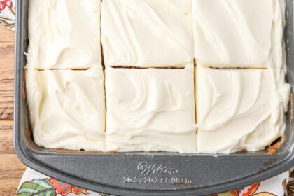 A horizontally aligned, top down close up photo of 6 slices of cake topped with fluffy cream cheese frosting in a metal pan.