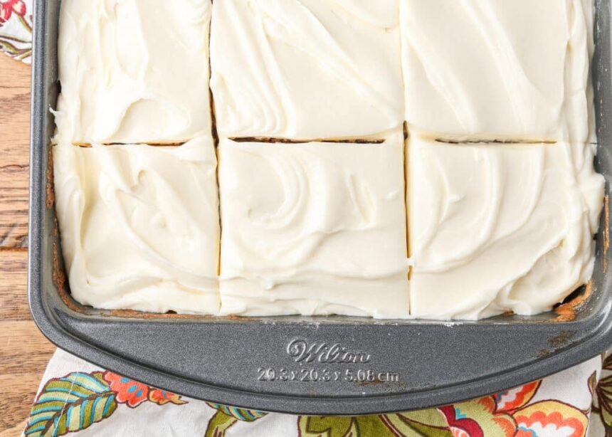 A horizontally aligned, top down close up photo of 6 slices of cake topped with fluffy cream cheese frosting in a metal pan.