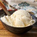 A close up shot of a serving of Mascarpone Ice Cream in a black ceramic bowl on a wooden table.
