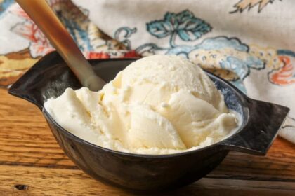 A close up shot of a serving of Mascarpone Ice Cream in a black ceramic bowl on a wooden table.