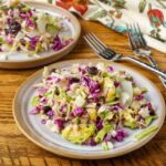 A horizontally aligned image of a ceramic plate piled high with shredded cabbage and sliced Brussels sprouts.