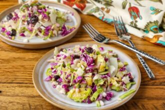 A horizontally aligned image of a ceramic plate piled high with shredded cabbage and sliced Brussels sprouts.
