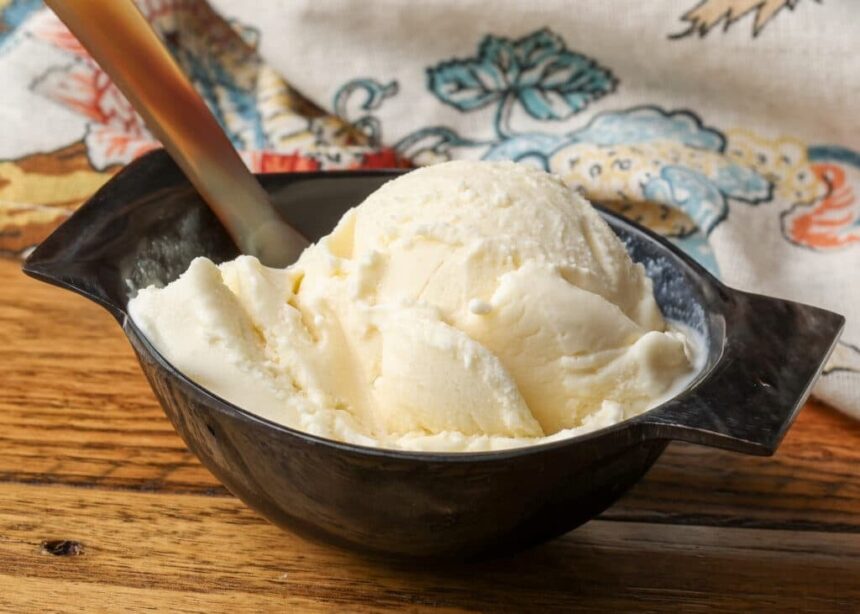 A close up shot of a serving of Mascarpone Ice Cream in a black ceramic bowl on a wooden table.