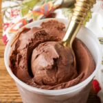 A horizontal photo of a freezer safe container on a wooden tabletop with a floral tea towel visible in the background.