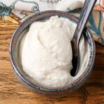 A horizontal close up of luscious white ice cream in a small grey bowl on a wooden tabletop.