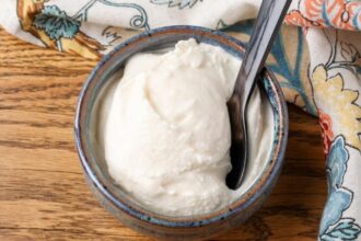 A horizontal close up of luscious white ice cream in a small grey bowl on a wooden tabletop.