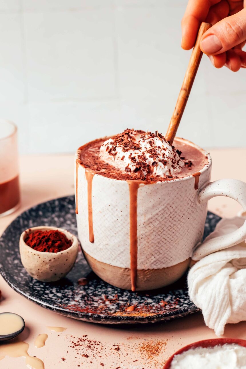 Small bowl of cocoa powder next to an overflowing mug of dairy-free tahini hot chocolate