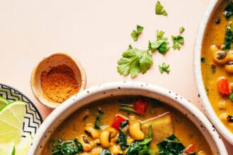 Overhead photo of a bowl of curried black eyed pea soup next to lime wedges, curry powder, and cornbread