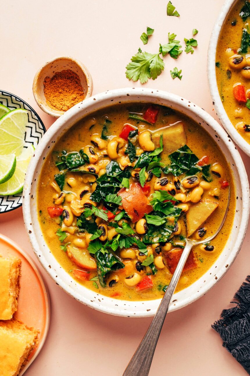 Overhead photo of a bowl of curried black eyed pea soup next to lime wedges, curry powder, and cornbread