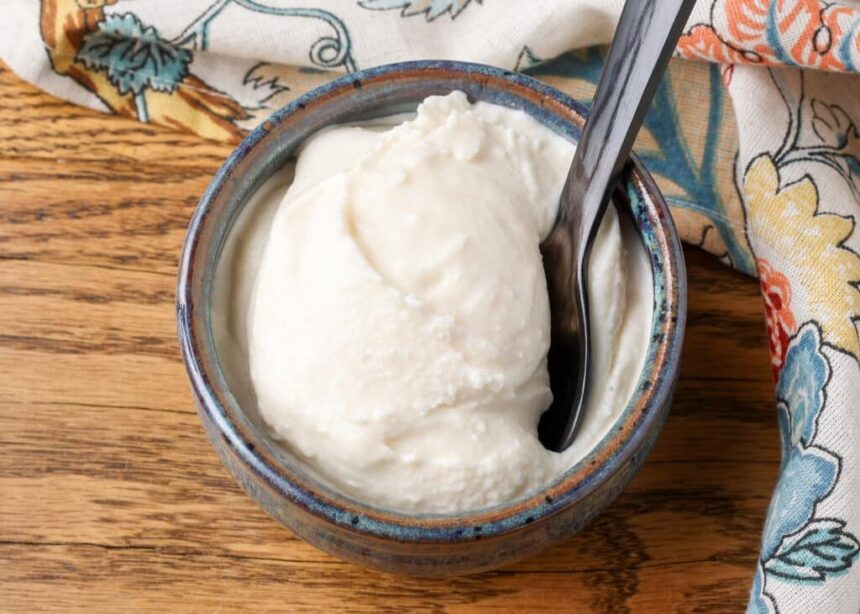 A horizontal close up of luscious white ice cream in a small grey bowl on a wooden tabletop.