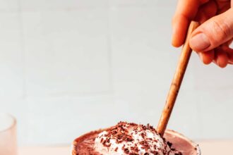 Small bowl of cocoa powder next to an overflowing mug of dairy-free tahini hot chocolate