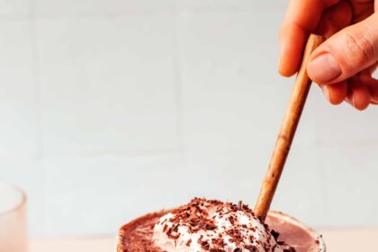 Small bowl of cocoa powder next to an overflowing mug of dairy-free tahini hot chocolate