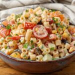 A horizontally aligned image showing a bowl of southwest pasta salad on a wooden tabletop.