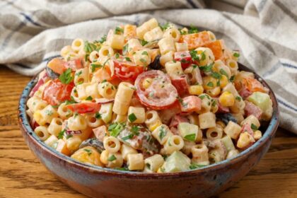 A horizontally aligned image showing a bowl of southwest pasta salad on a wooden tabletop.