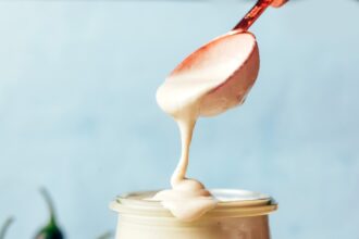 Creamy vegan cashew jalapeño dressing dripping off a spoon into a glass jar